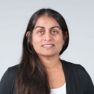 iuGO Digital - A woman with long brown hair wearing a black cardigan over a light-colored top, facing the camera with a neutral expression against a plain background.